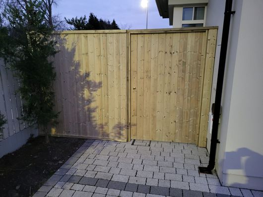 A wooden fence is next to a brick walkway