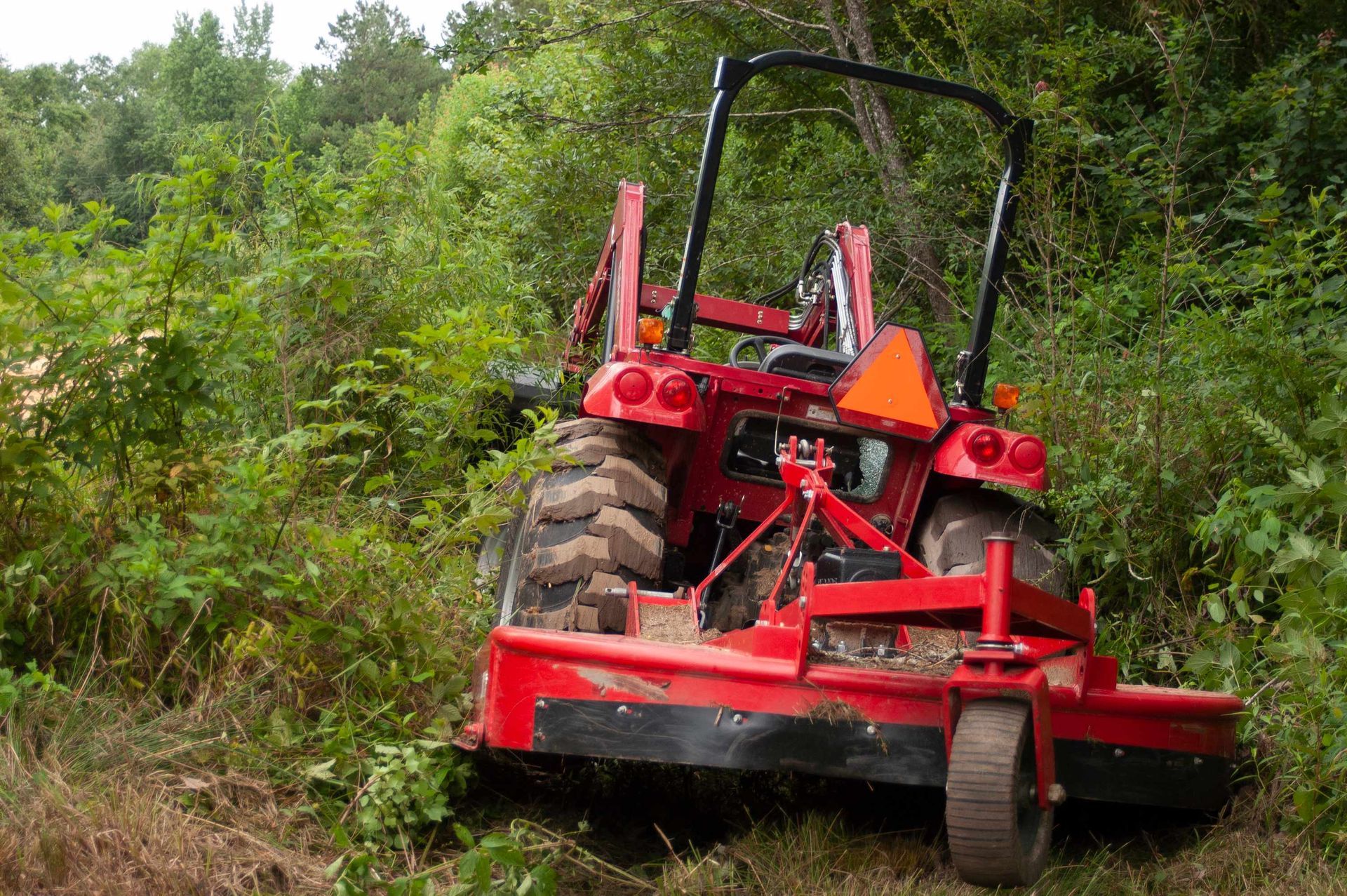 Red tractor mower cutting grass on a steep, overgrown hillside path