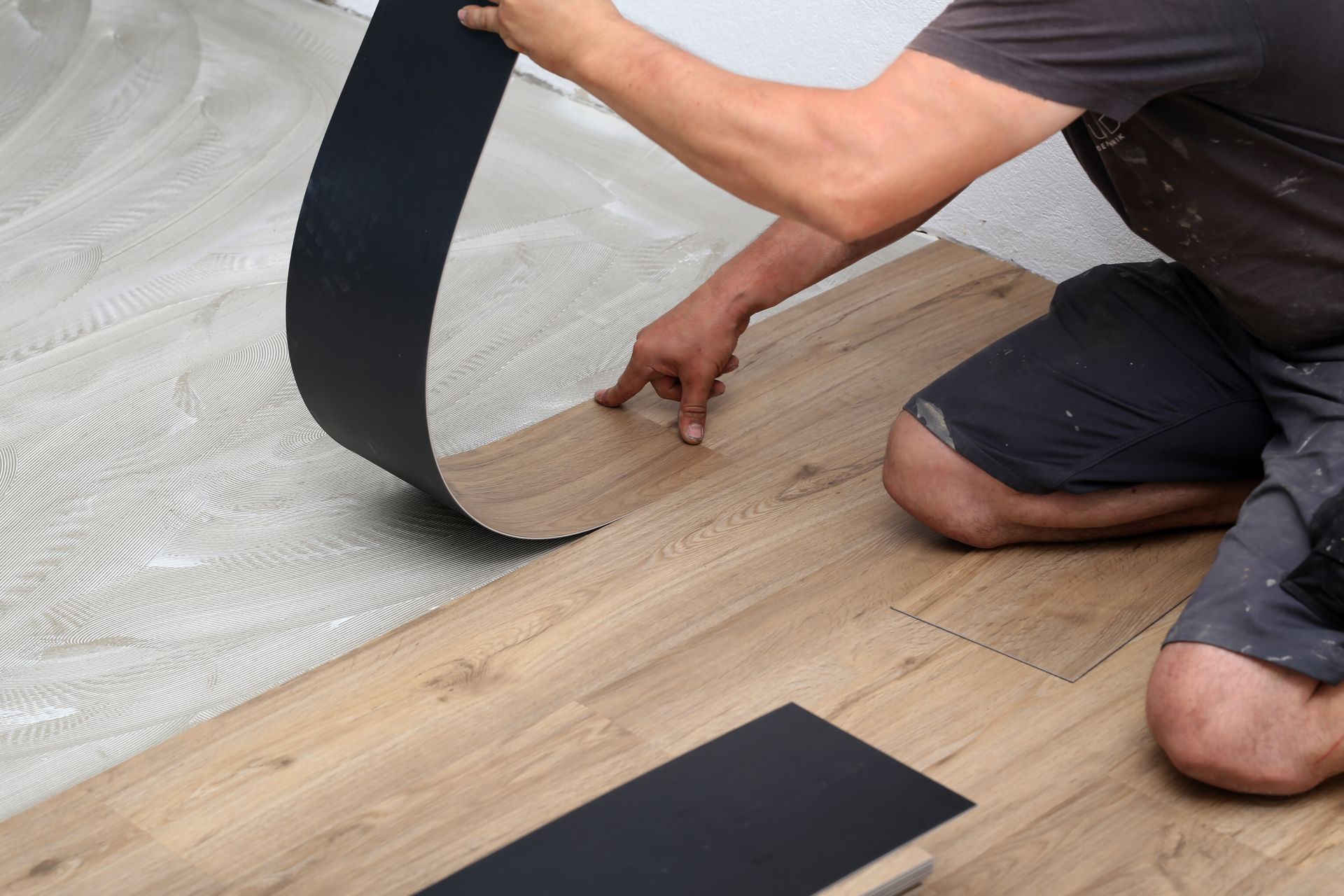 Person installing wood-look flooring, peeling back a black adhesive strip.