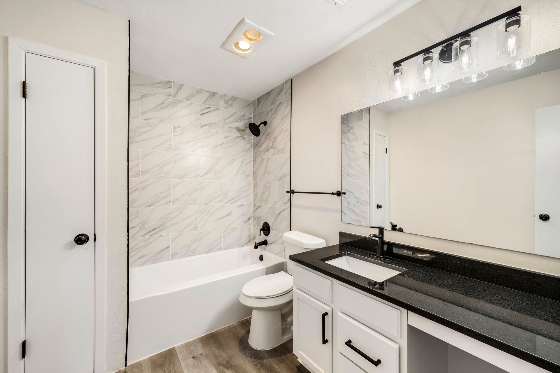 Bathroom with white vanity, black countertop, tub, and toilet.