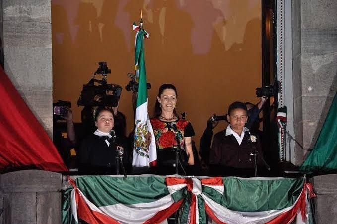 Mexico City mayor waving from balcony, flanked by children, Mexican flags.