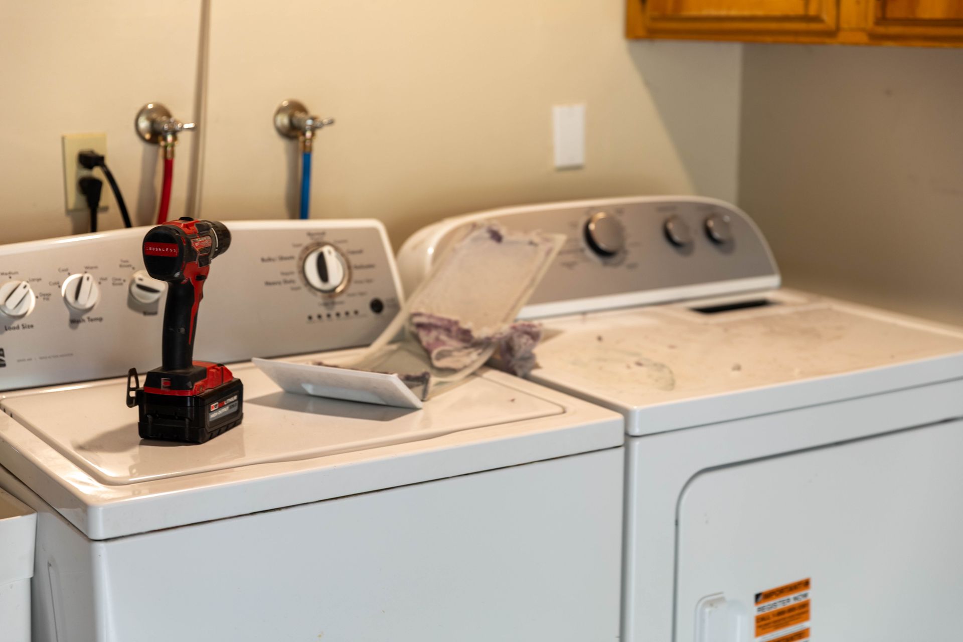 A person in a blue button-down shirt cleaning a dryer vent hose with a vacuum attachment in a laundry room.
