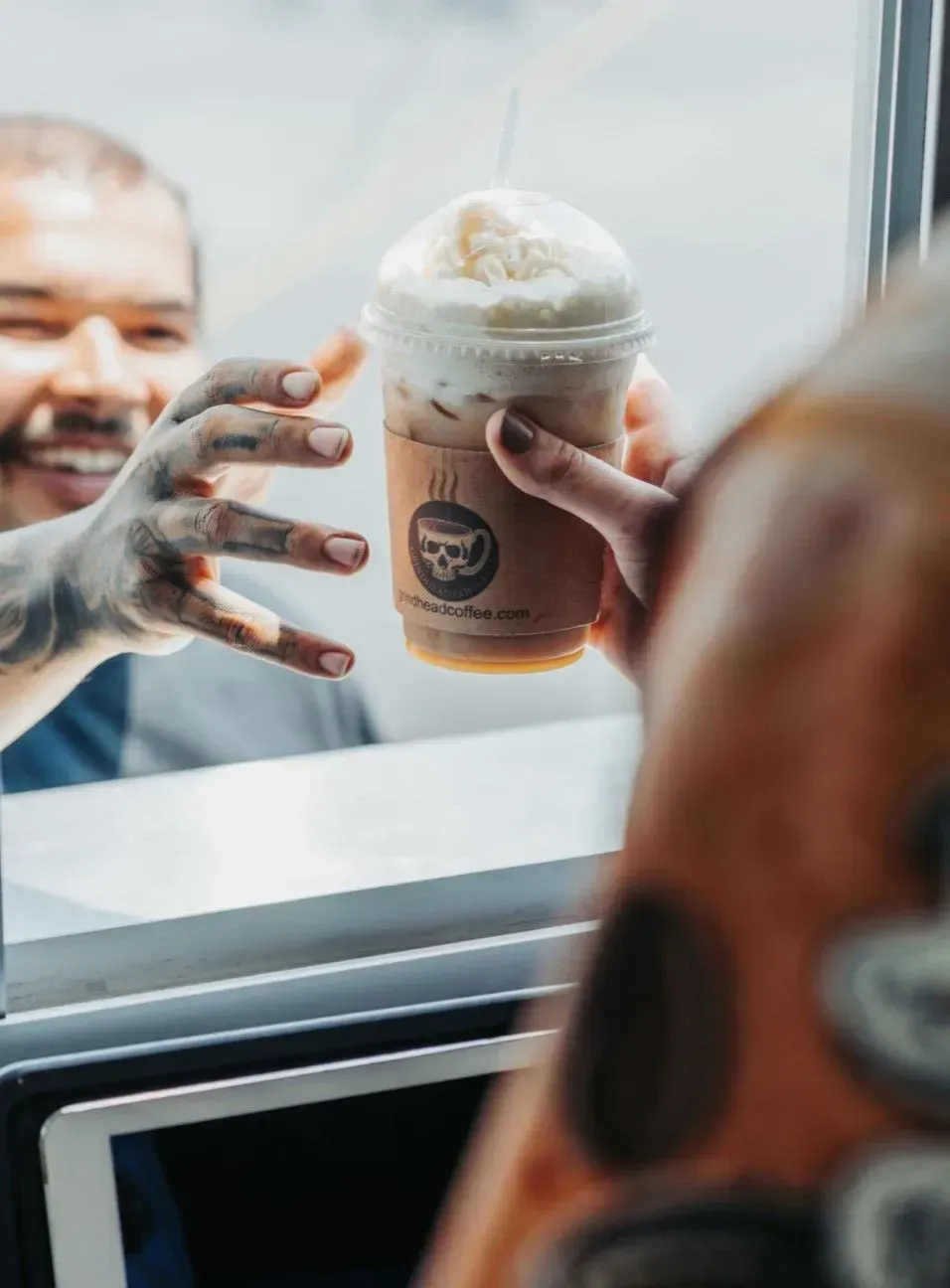 Hand reaching through a window to hand a lidded iced coffee to a smiling customer