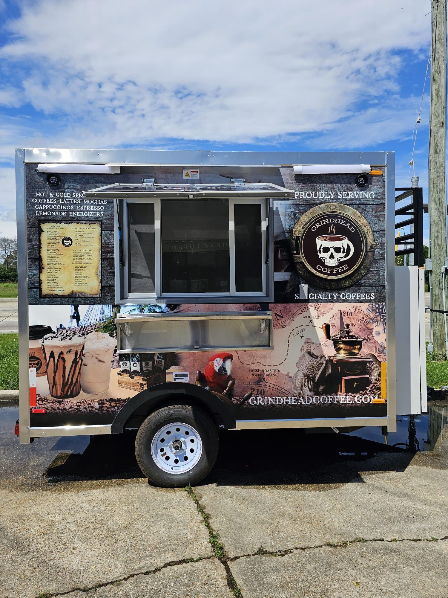 Customized food truck with menu window and logos parked outdoors on a sunny day