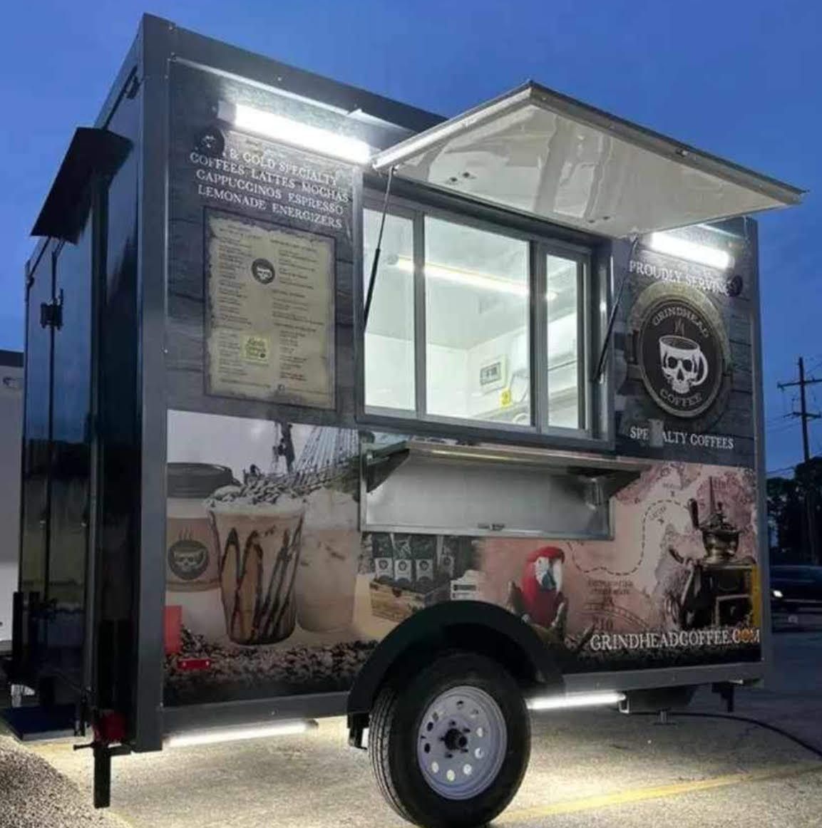 Black food truck trailer with serving window and lit menu boards at dusk