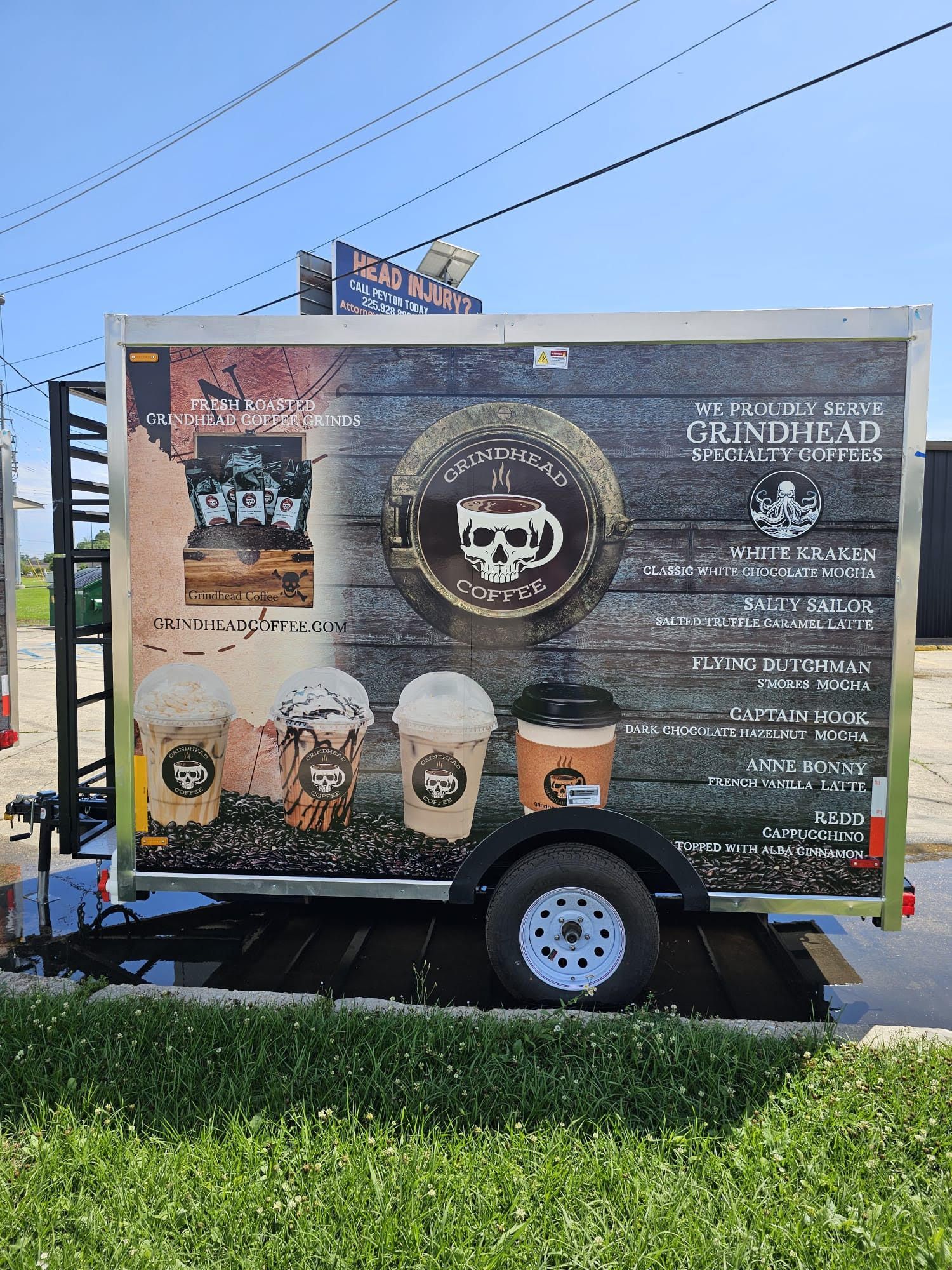 Traded trailer billboard advertising craft beer and drinks, parked on grass beside a road.