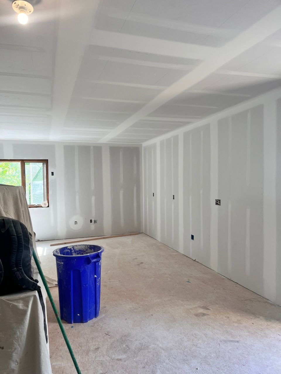 A large room with white walls and a blue trash can in the middle.