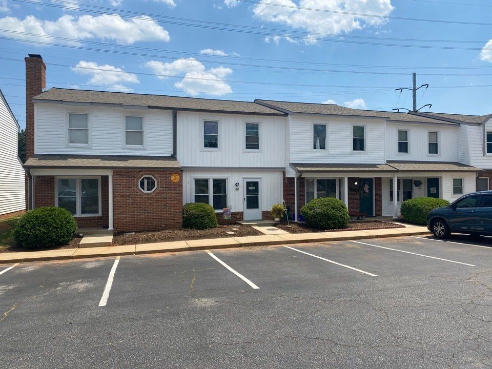 Row of white and brick townhouses with parking spaces under a blue sky