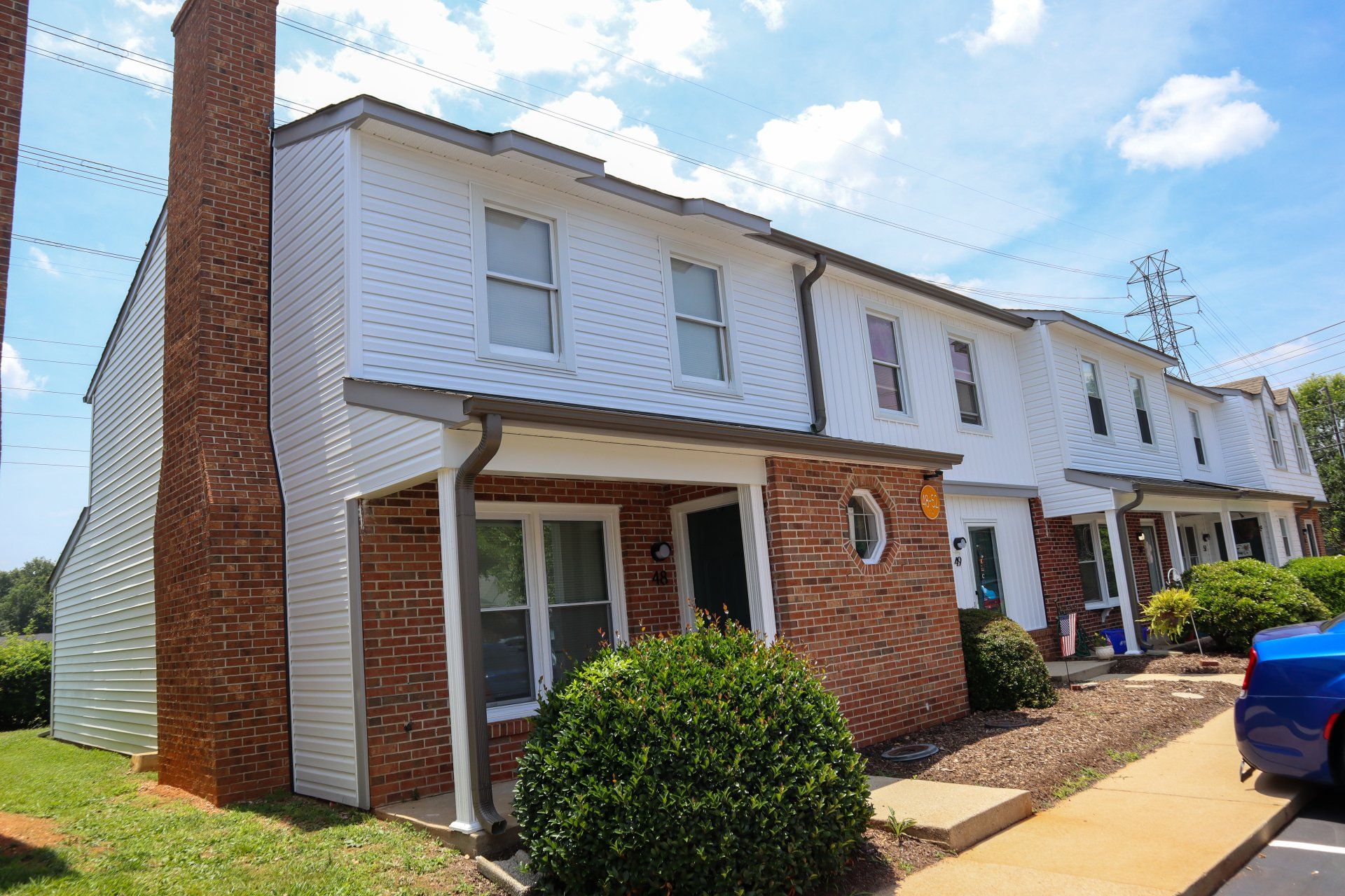 Row of brick-and-white townhouses on a sunny street, with a blue car parked at the curb.