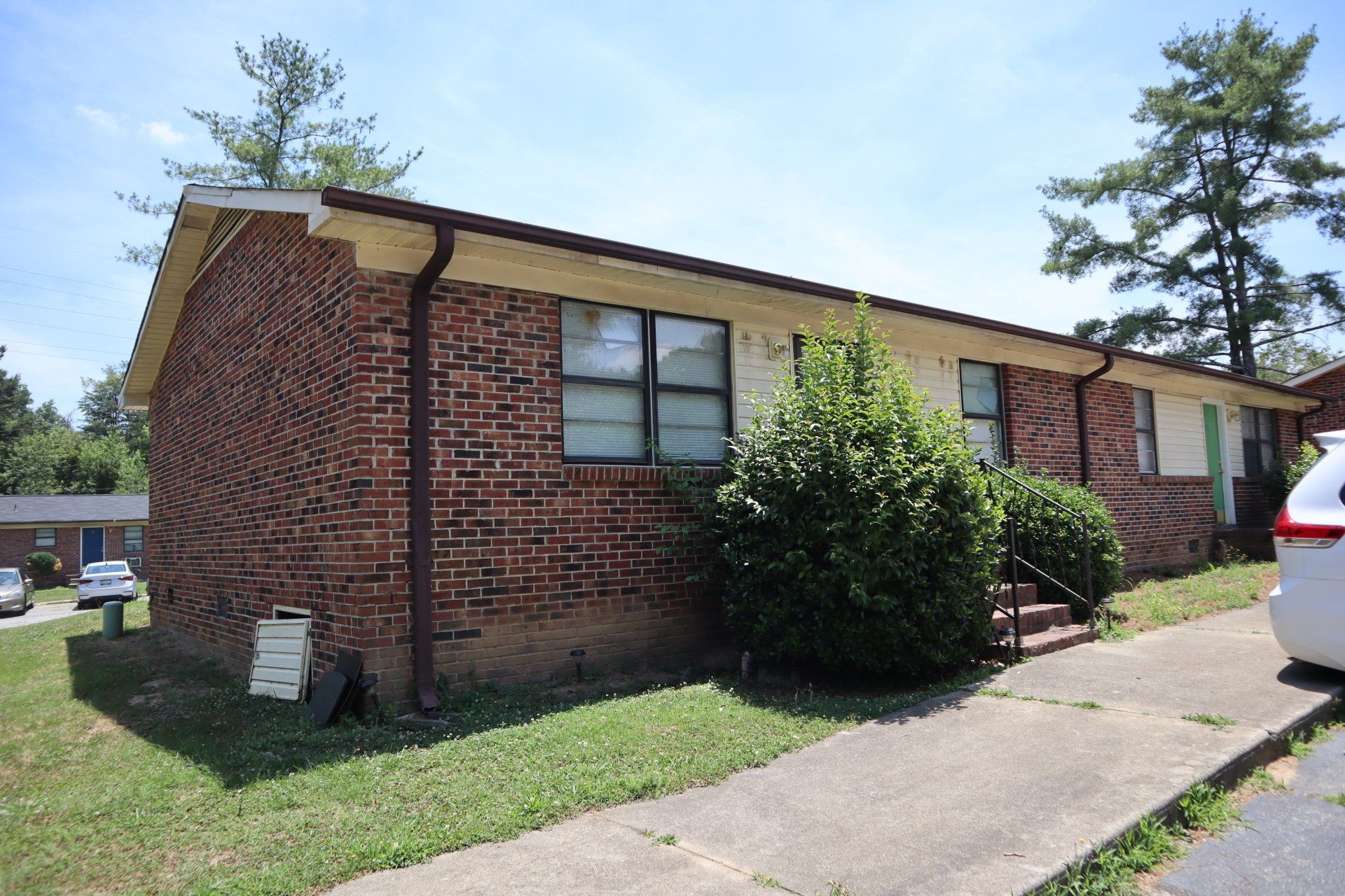 Brick apartment building with brown trim, green bushes, and a concrete walkway.