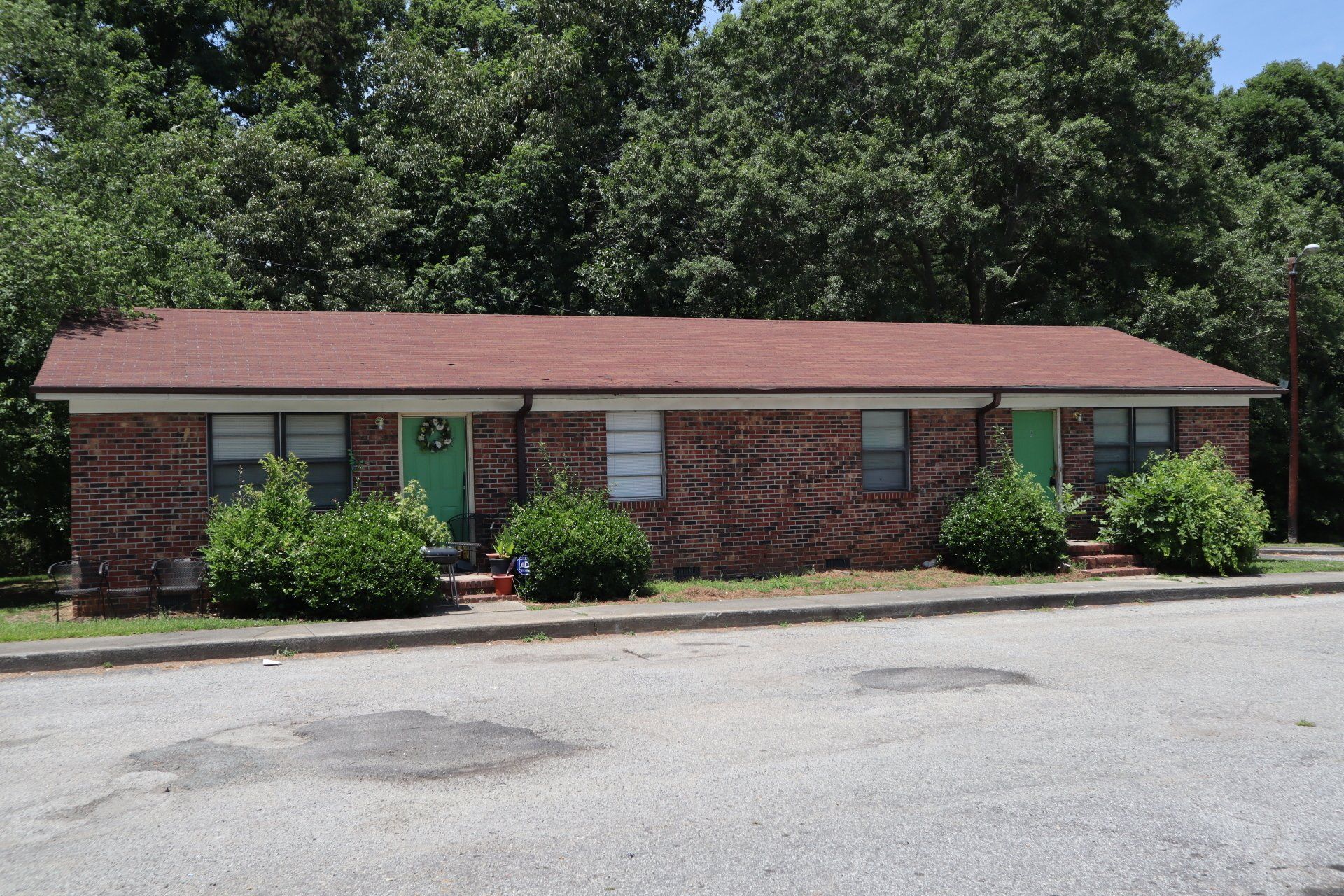 Two brick apartment units with green doors, set in front of trees.
