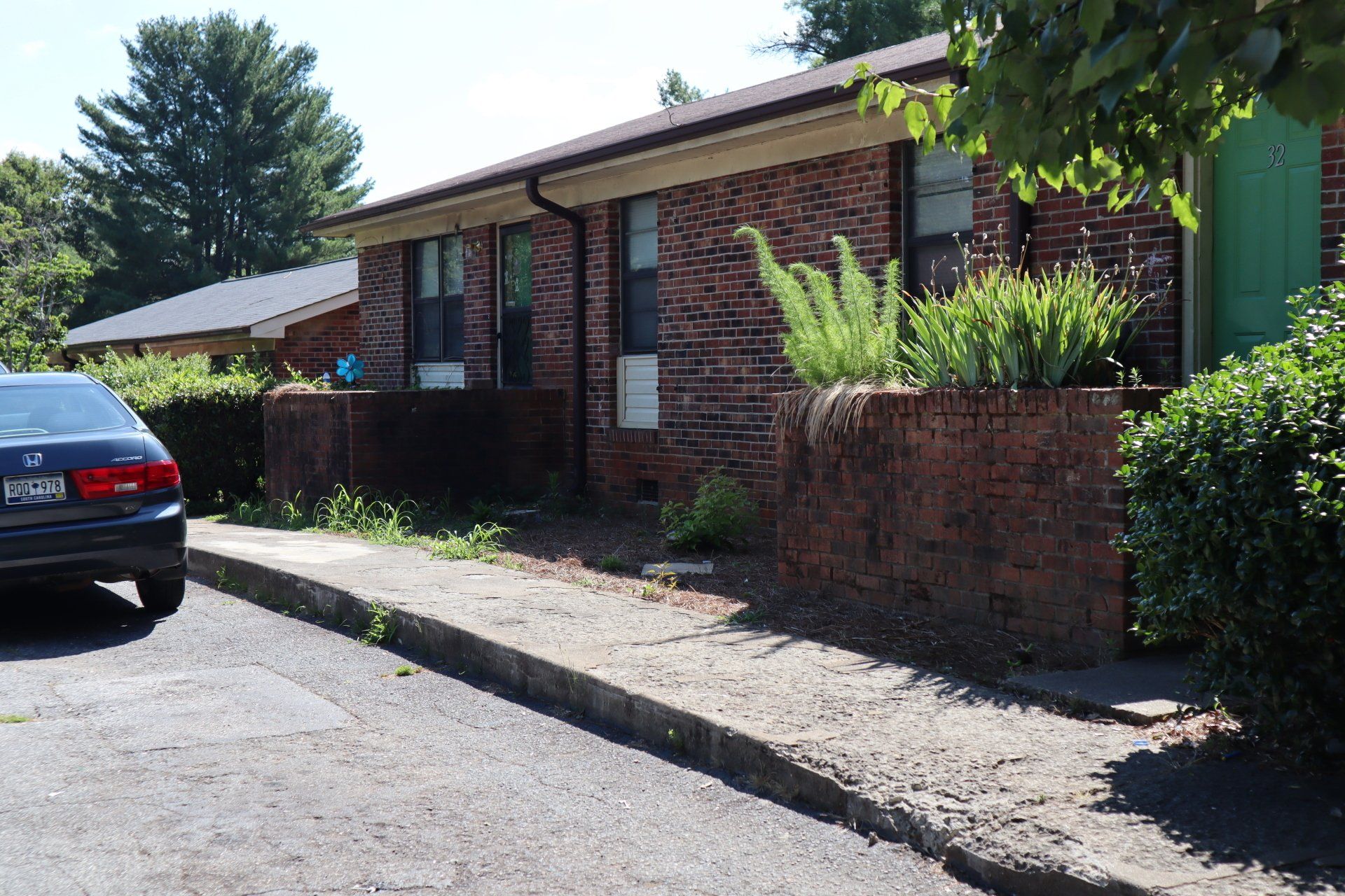 Low brick wall with plants in front of a brick building with a car parked nearby.