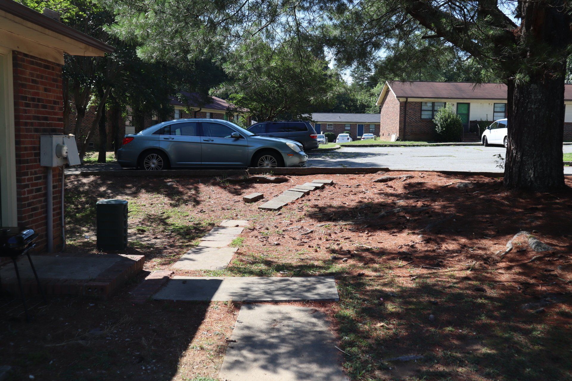 Brick building exterior with a parked gray car in front. Pathway to the building.