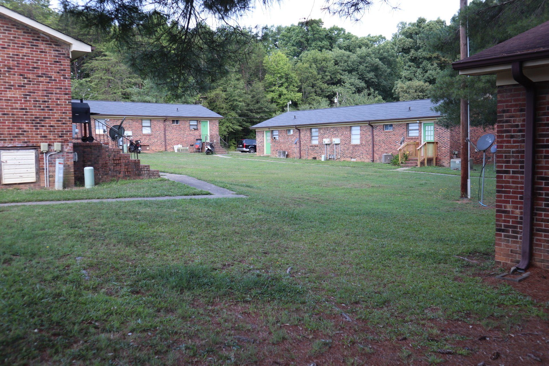 Low-rise brick apartment buildings with green doors sit on a grassy lawn with trees in the background.