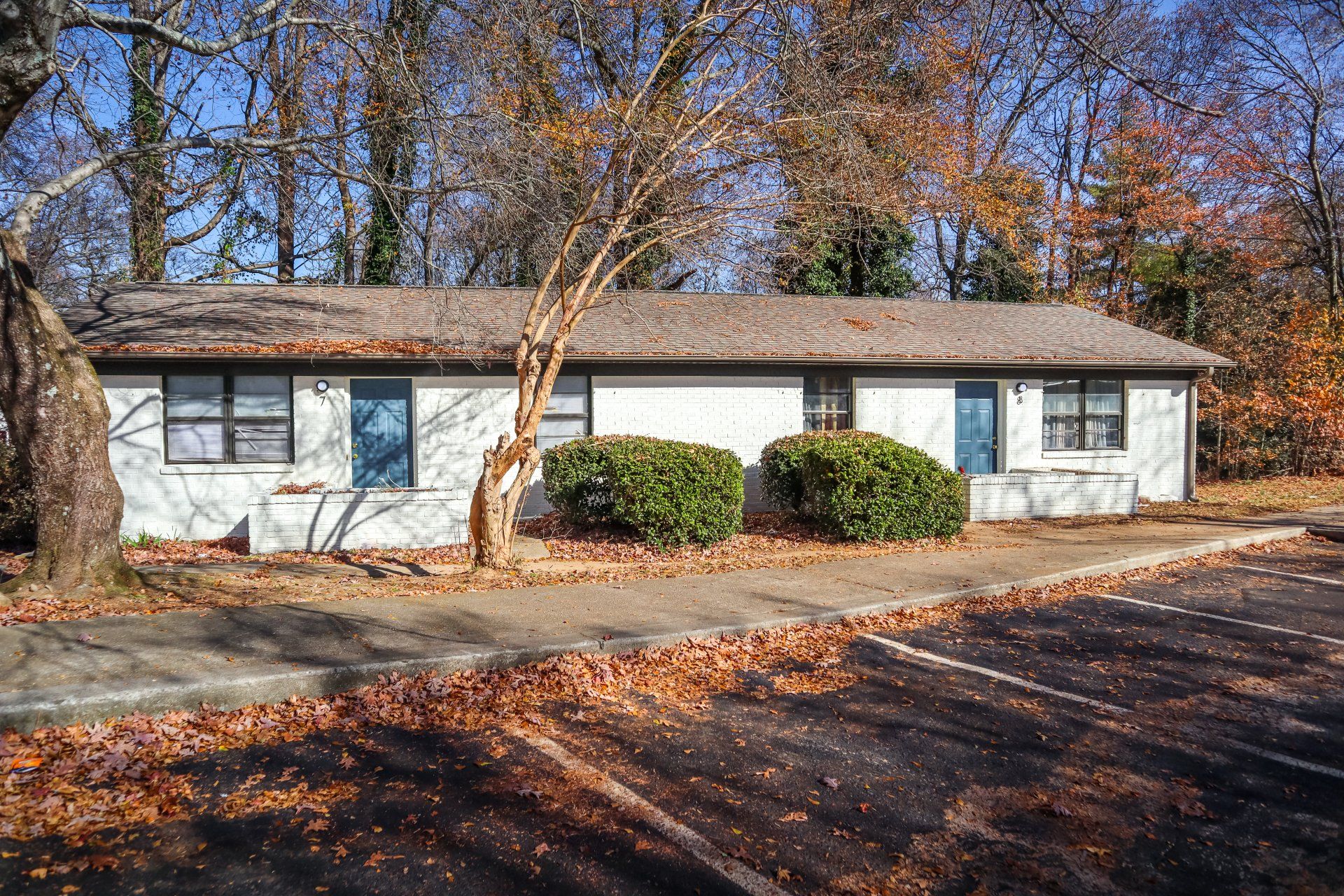 Single-story white brick building with blue doors, brown roof, and fall foliage.