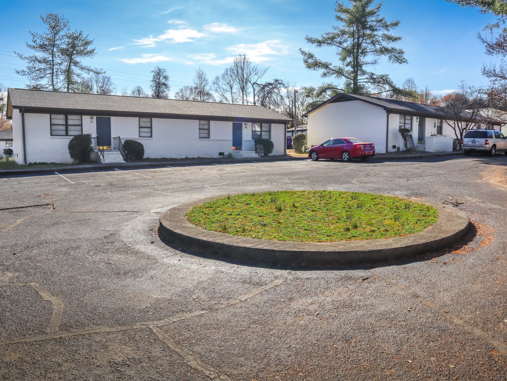 Exterior view of white apartment buildings with a small roundabout. Red car parked nearby.