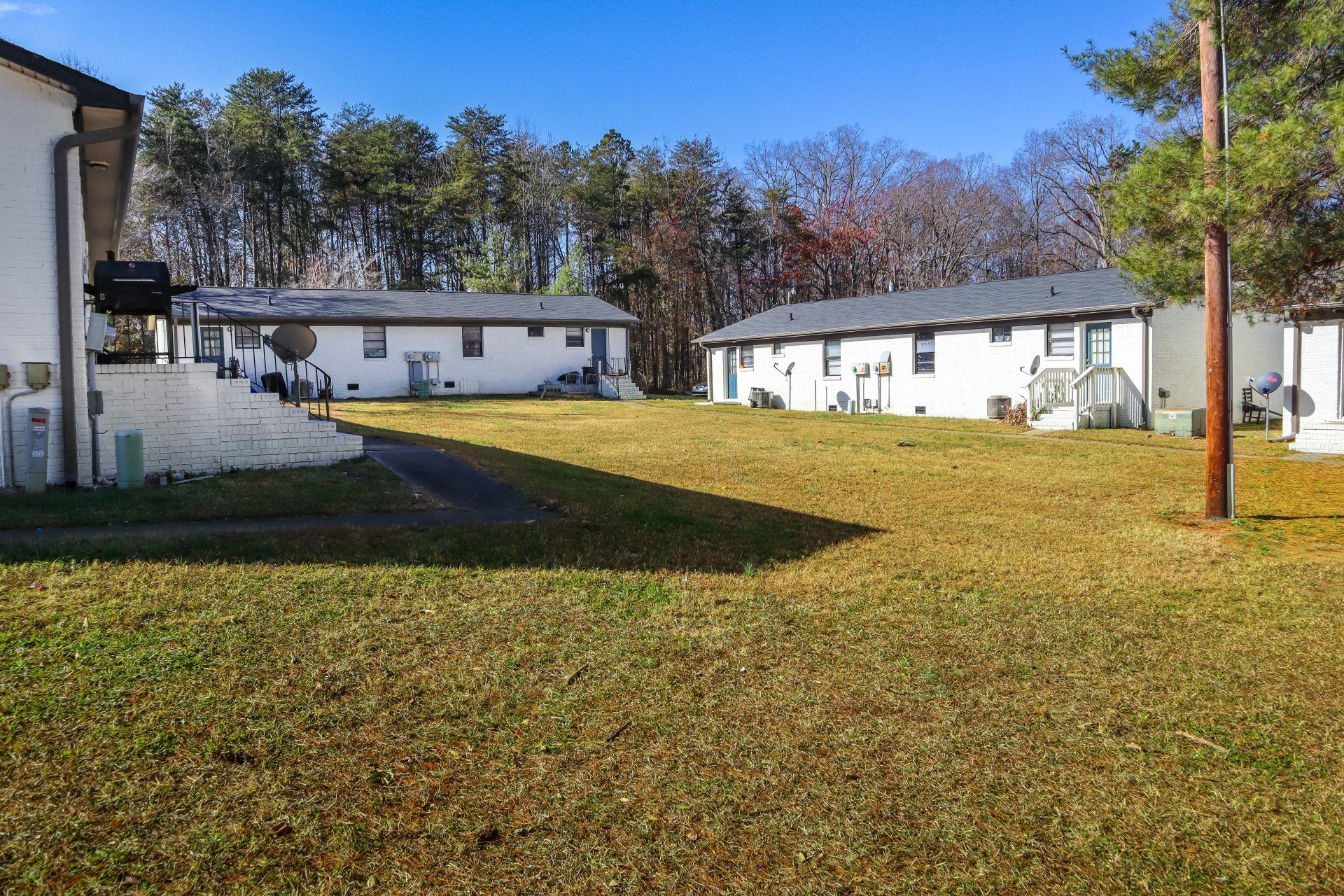 Grassy yard with several white buildings in the background under a blue sky.