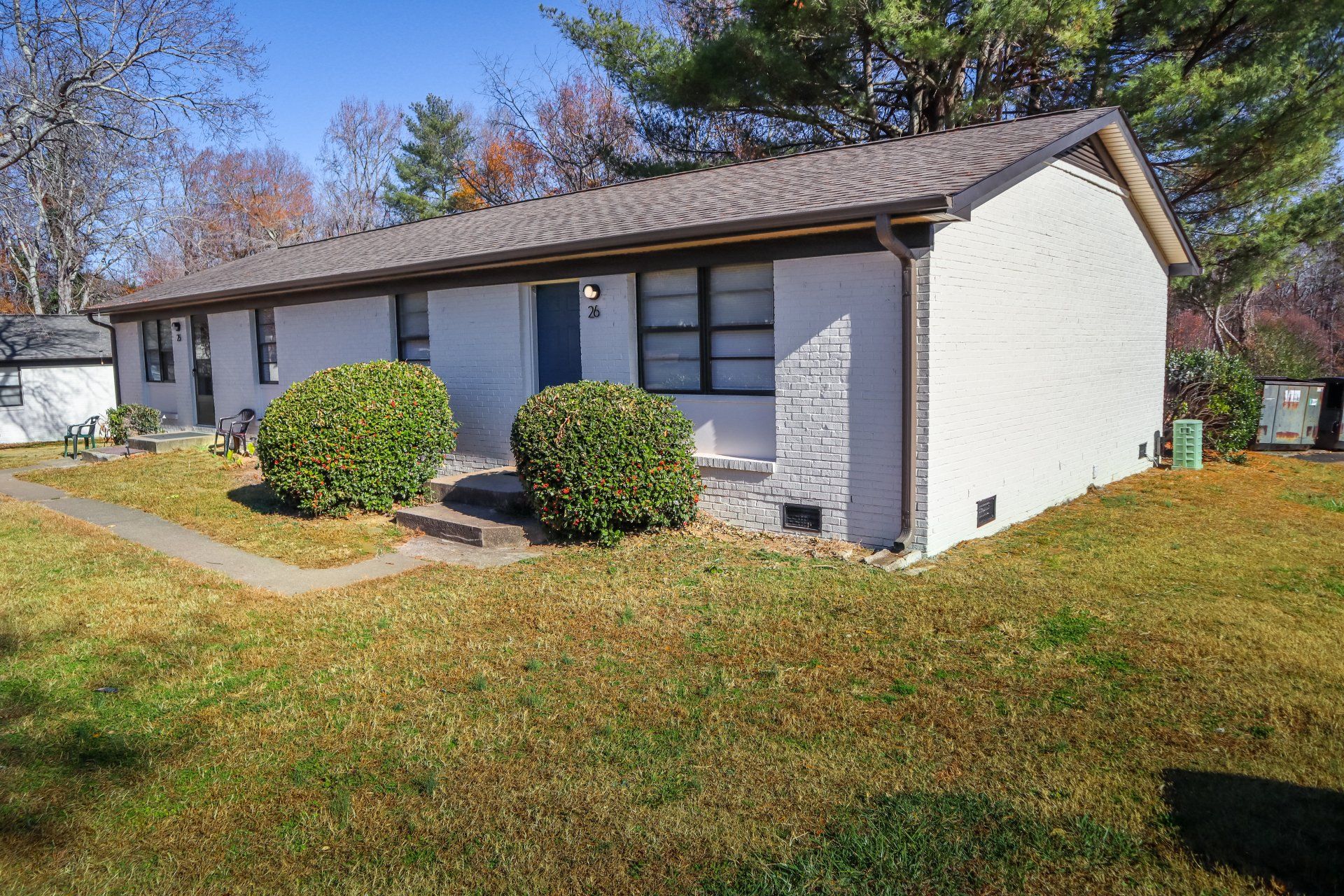 White brick building with brown roof, front yard of grass and shrubs, blue door.