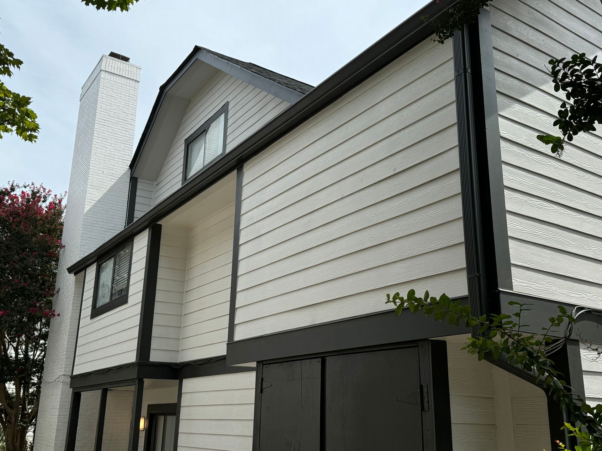 Two-story white house with black trim and a brick chimney viewed from below
