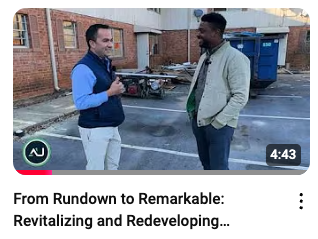 Two men conversing outdoors in front of a building undergoing renovation. One gestures with a thumbs-up.