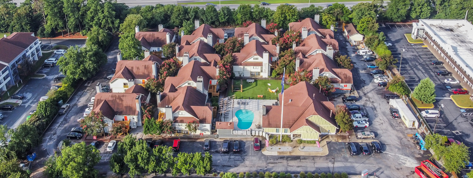Aerial view of a residential complex with red roofs, a swimming pool, and surrounding greenery.