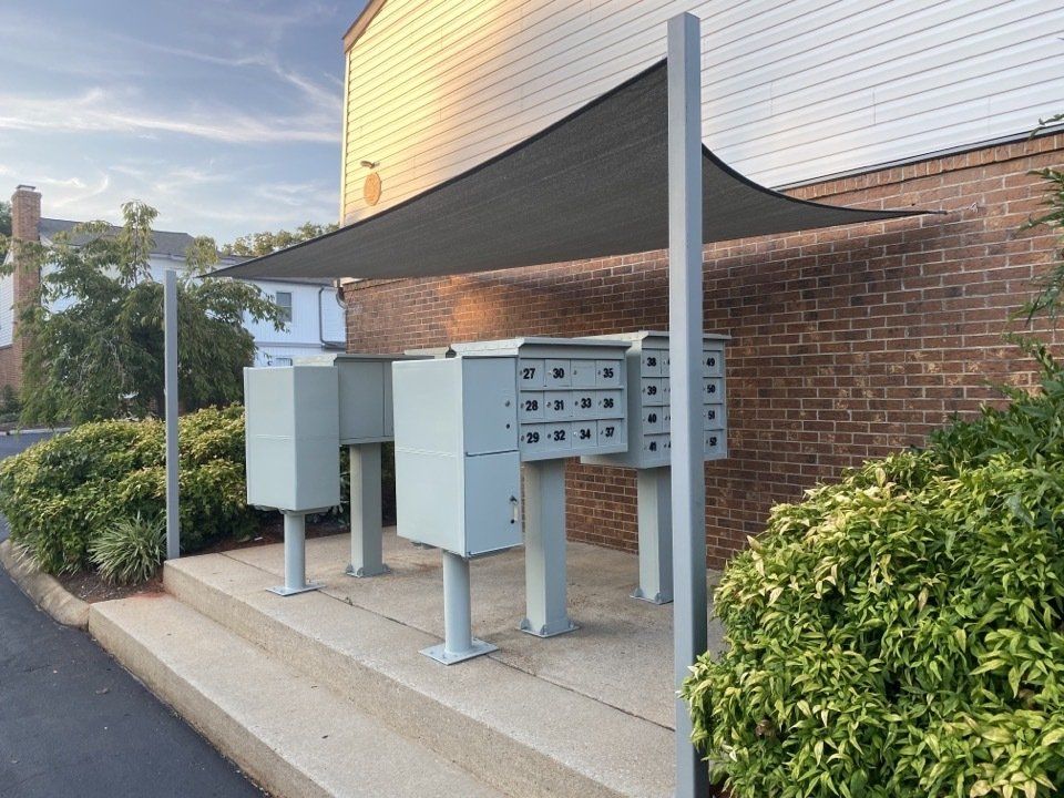 Outdoor cluster of gray utility boxes and mailboxes under a canopy beside a brick building