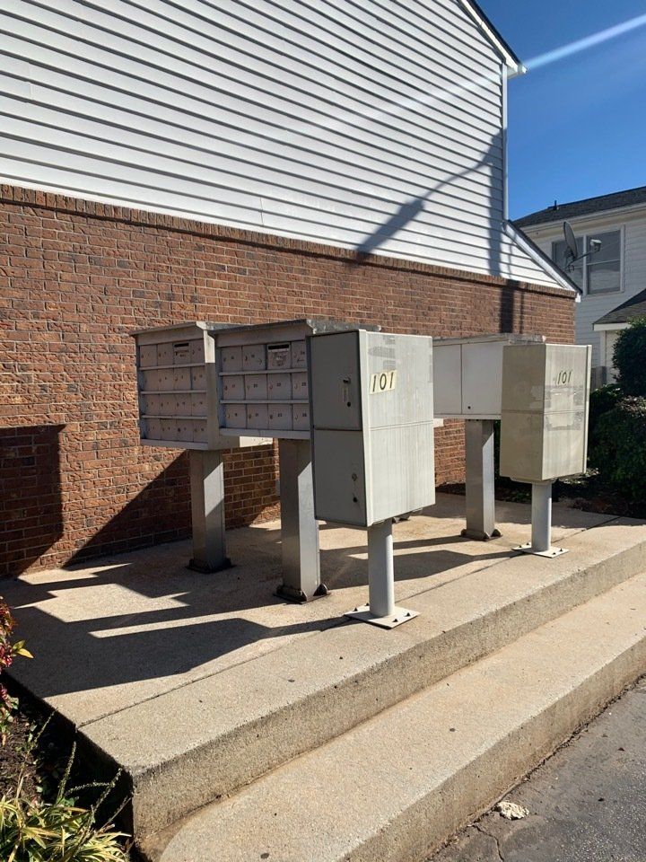 Cluster of outdoor mailboxes mounted on posts beside a brick building and concrete sidewalk.