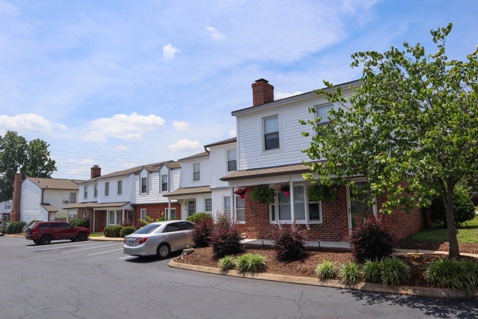 Row of suburban townhouses with parked cars and a tree-lined street under a blue sky