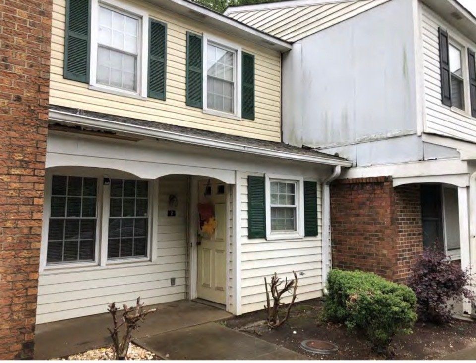 Two-story townhouse exterior with beige siding, brick accents, and a small front porch