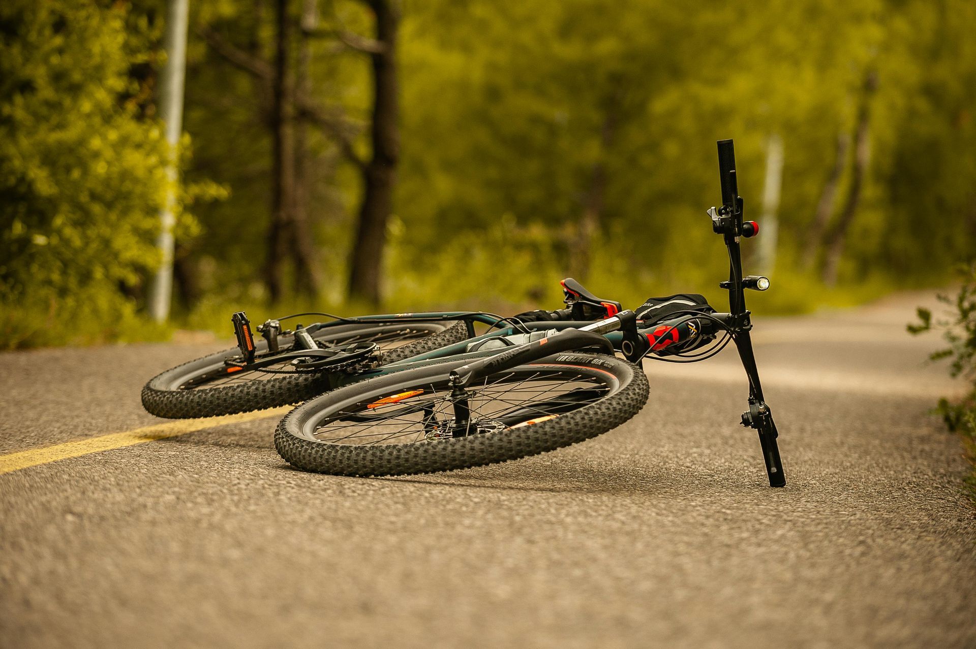 Mountain bike lying on its side on a forest road, with blurred trees in the background.