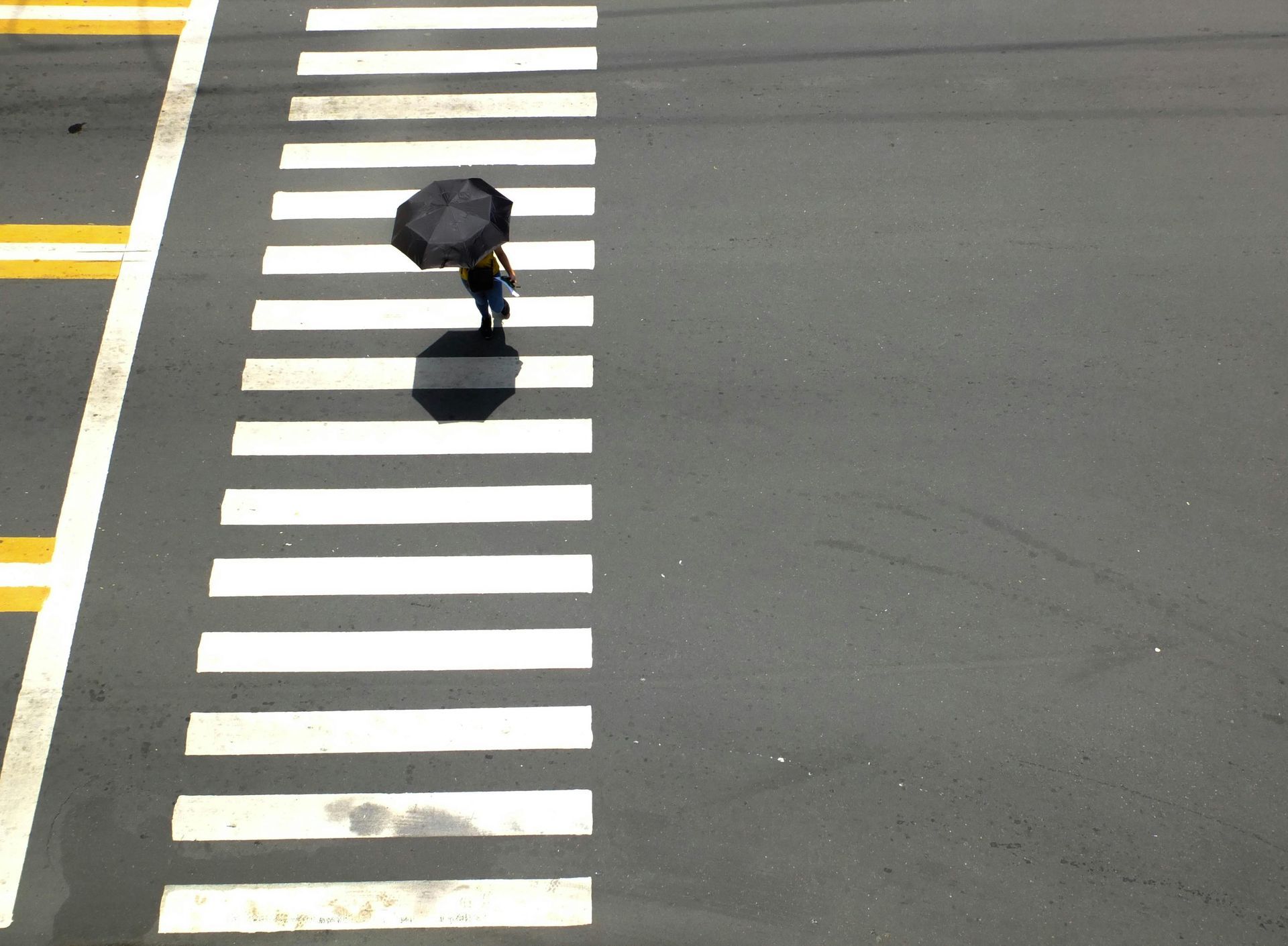 Person with black umbrella crossing a striped crosswalk on a gray road.