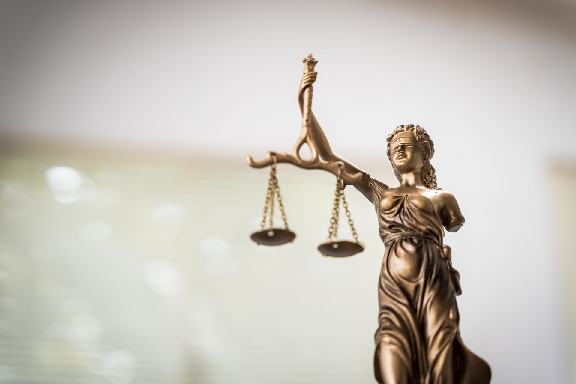 Lady Justice statue holding scales against a blurred courtroom background