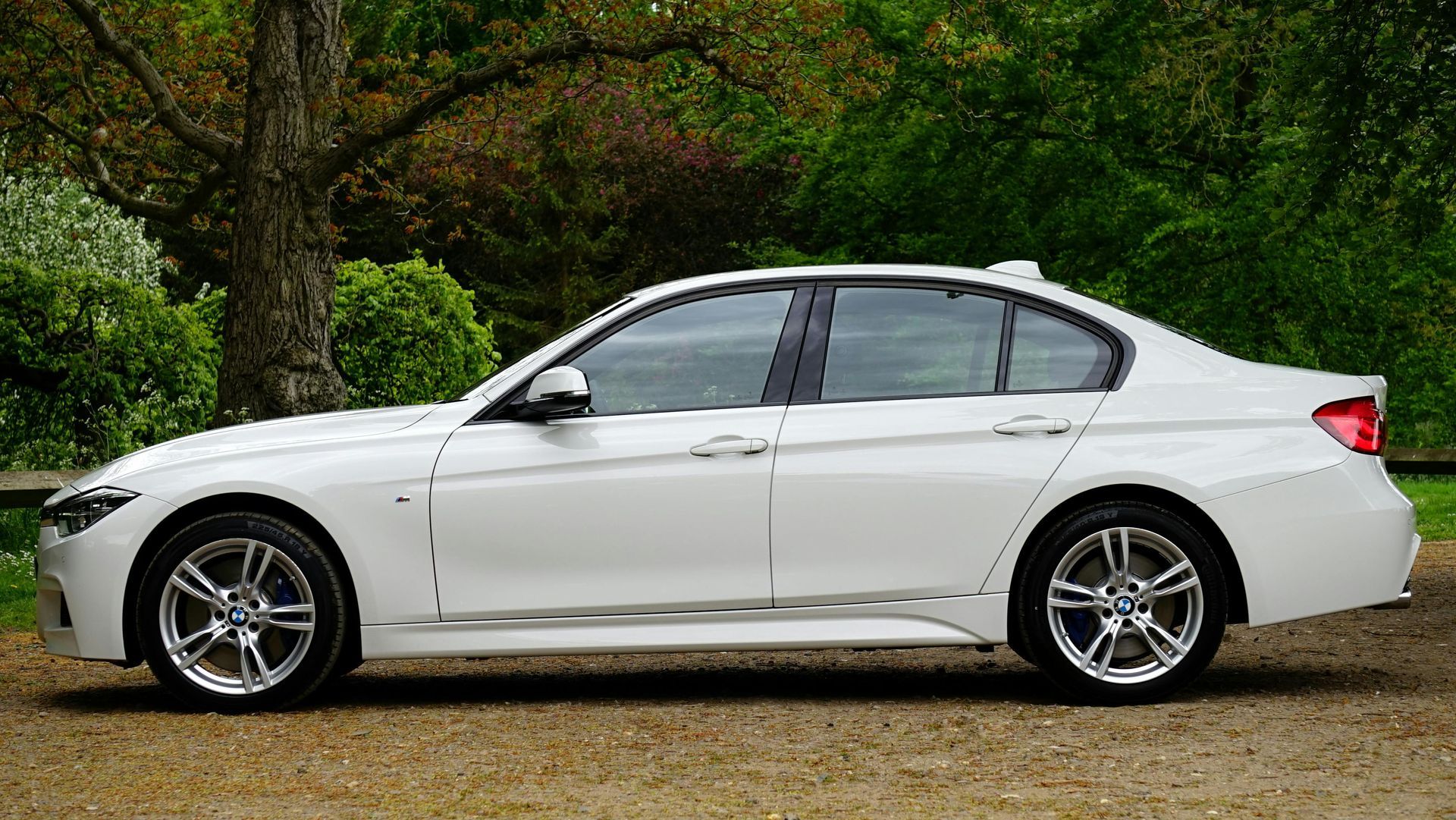 White BMW sedan parked on gravel with trees in the background.