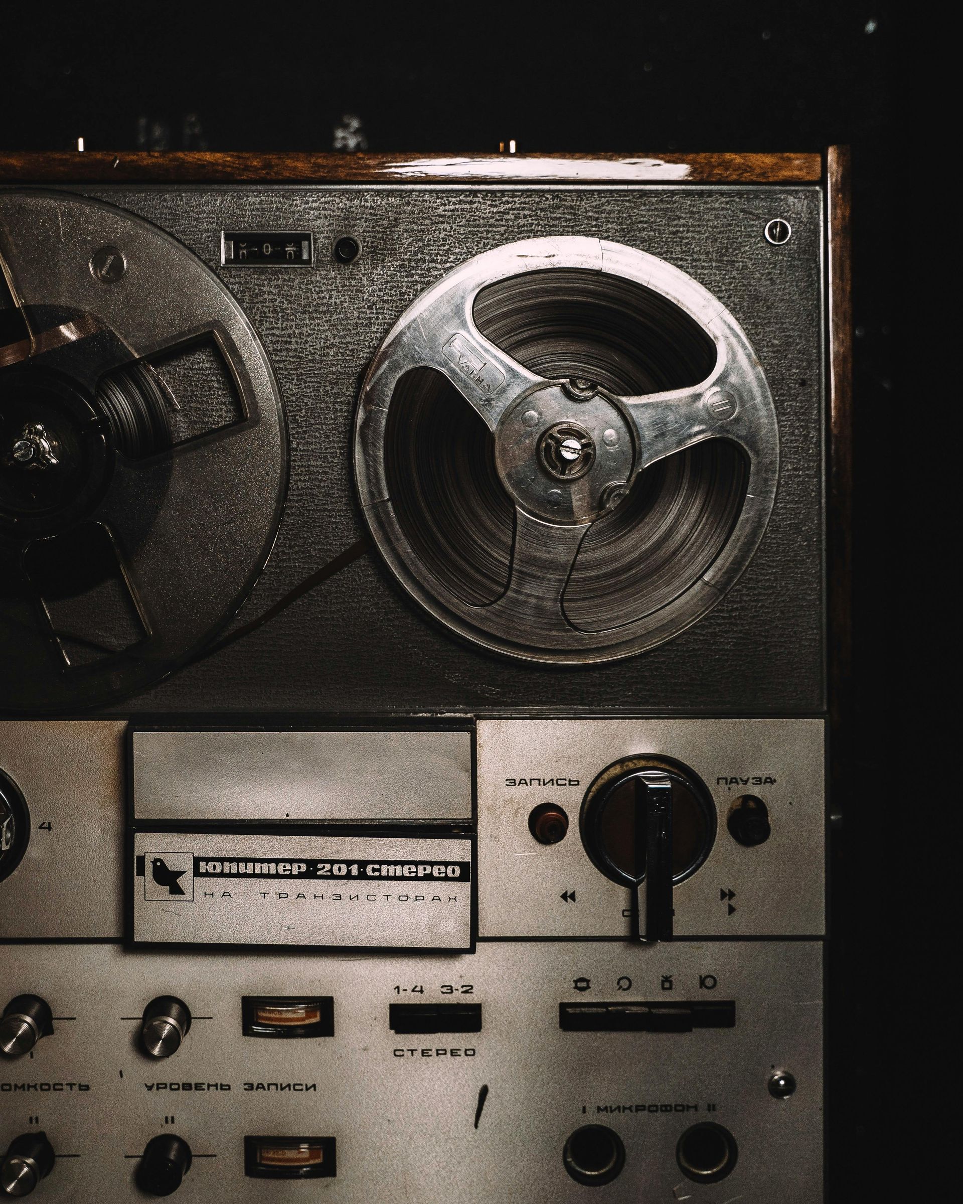 Vintage reel-to-reel tape recorder. Silver and wood tones against a dark background.