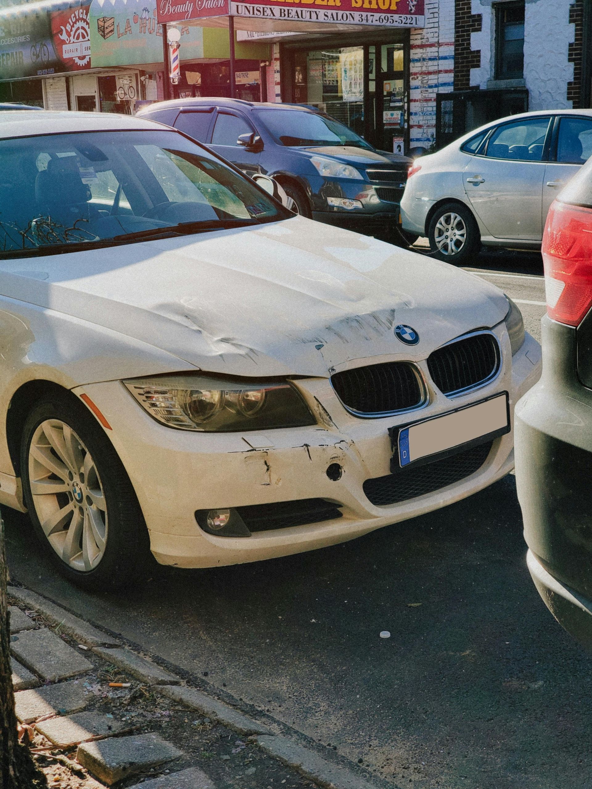 White BMW car with front-end damage parked on a street.
