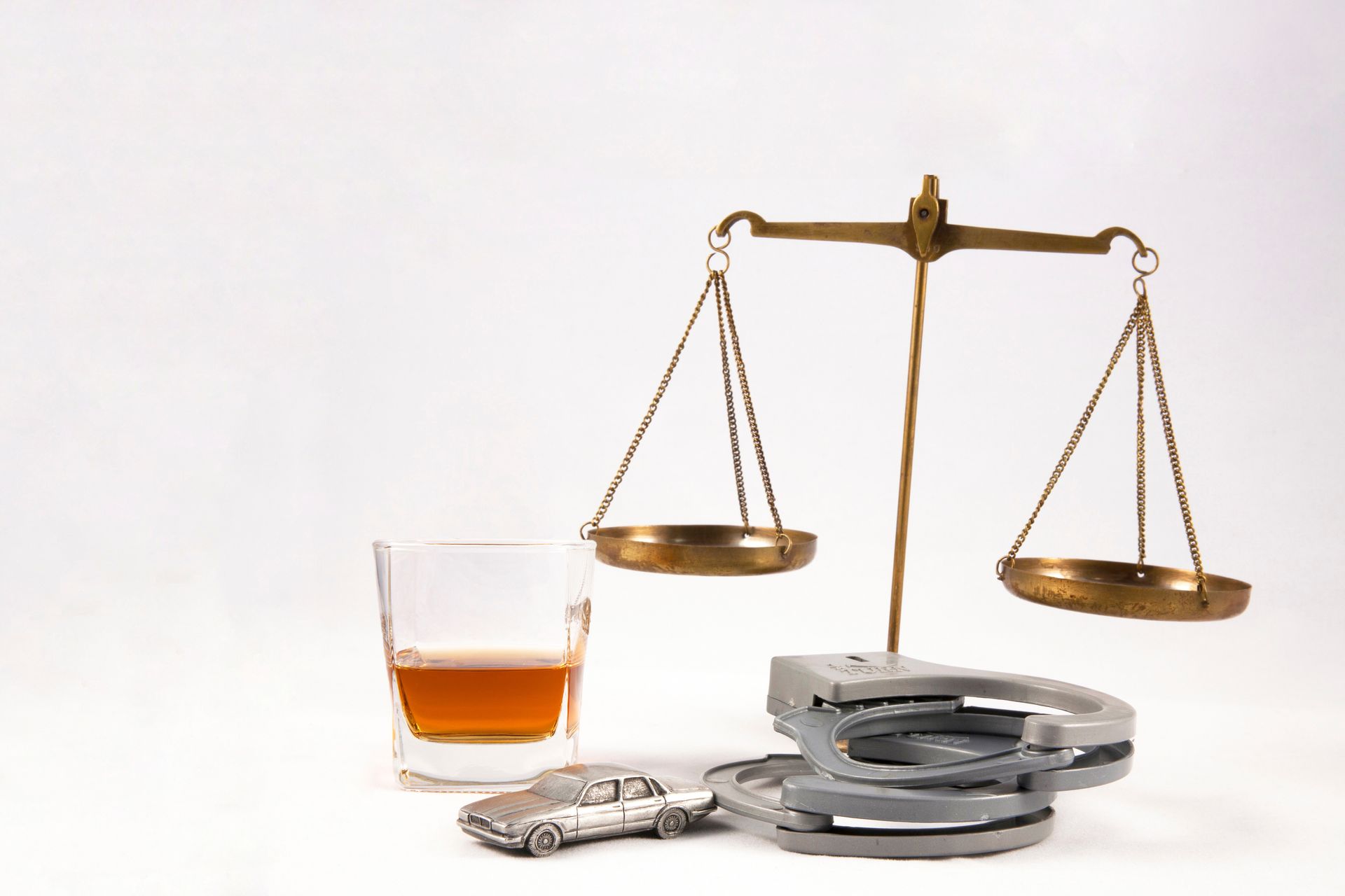 A glass and a pair of handcuffs, next to a pair of golden scales. A glass and a pair of handcuffs, next to a pair of golden scales.