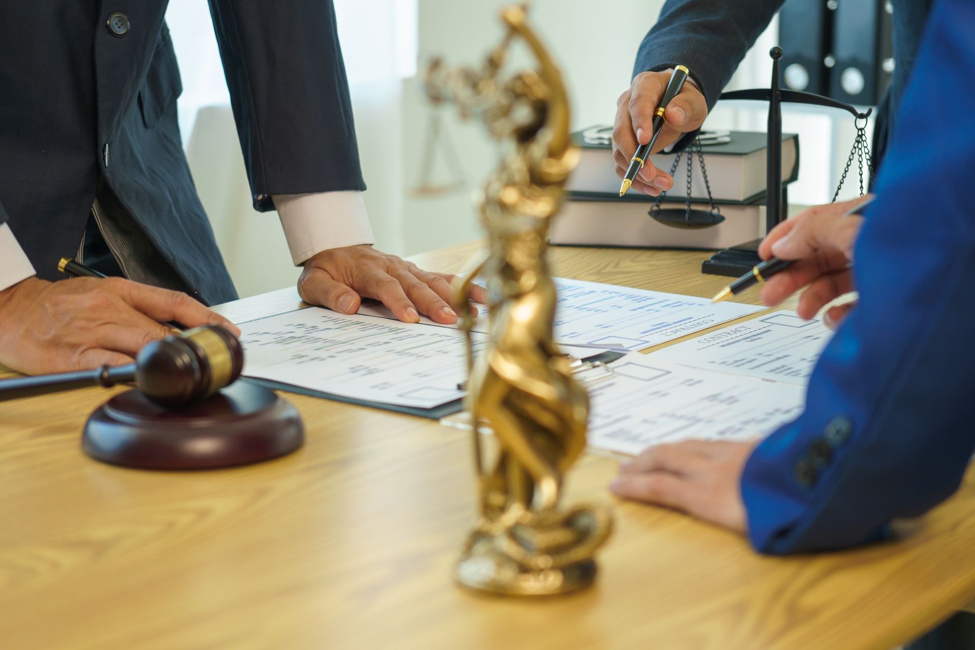 Three lawyers review court documents on a desk with a Lady Justice statue, gavel, and books.