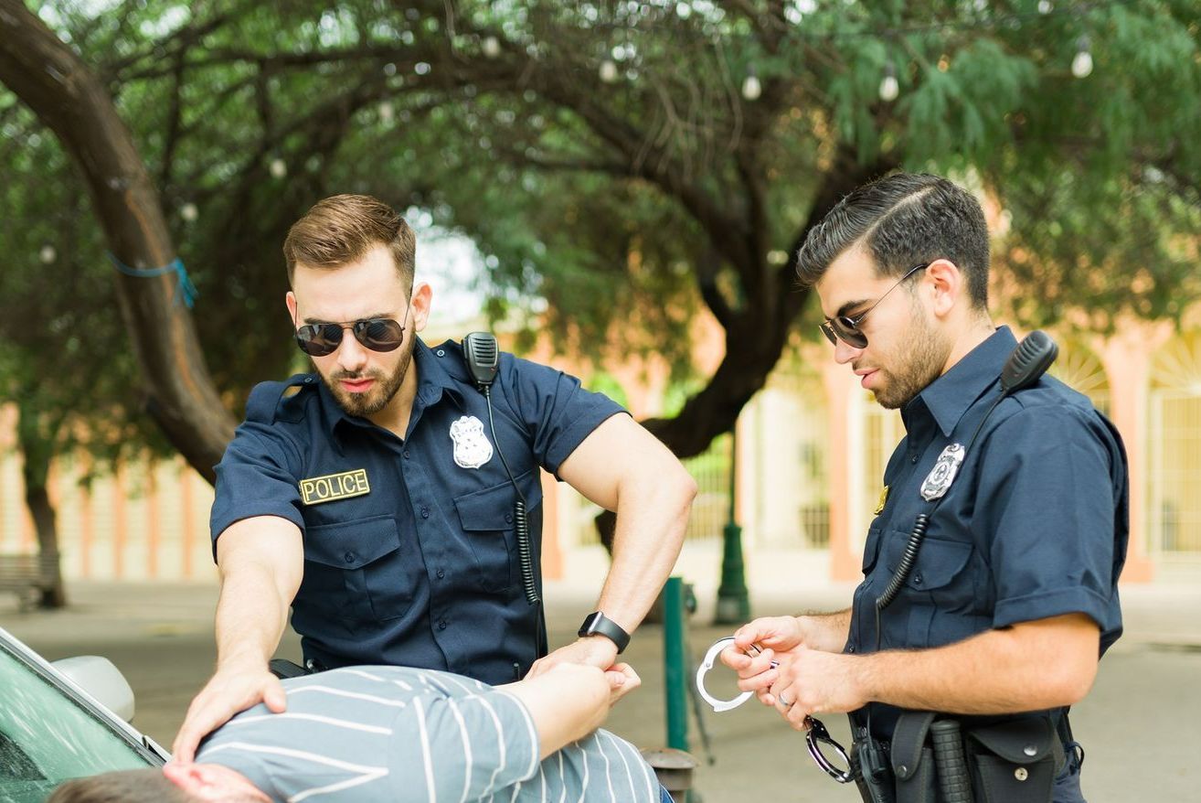 Two police officers are arresting a man in a parking lot. Two police officers are arresting a man in a parking lot.