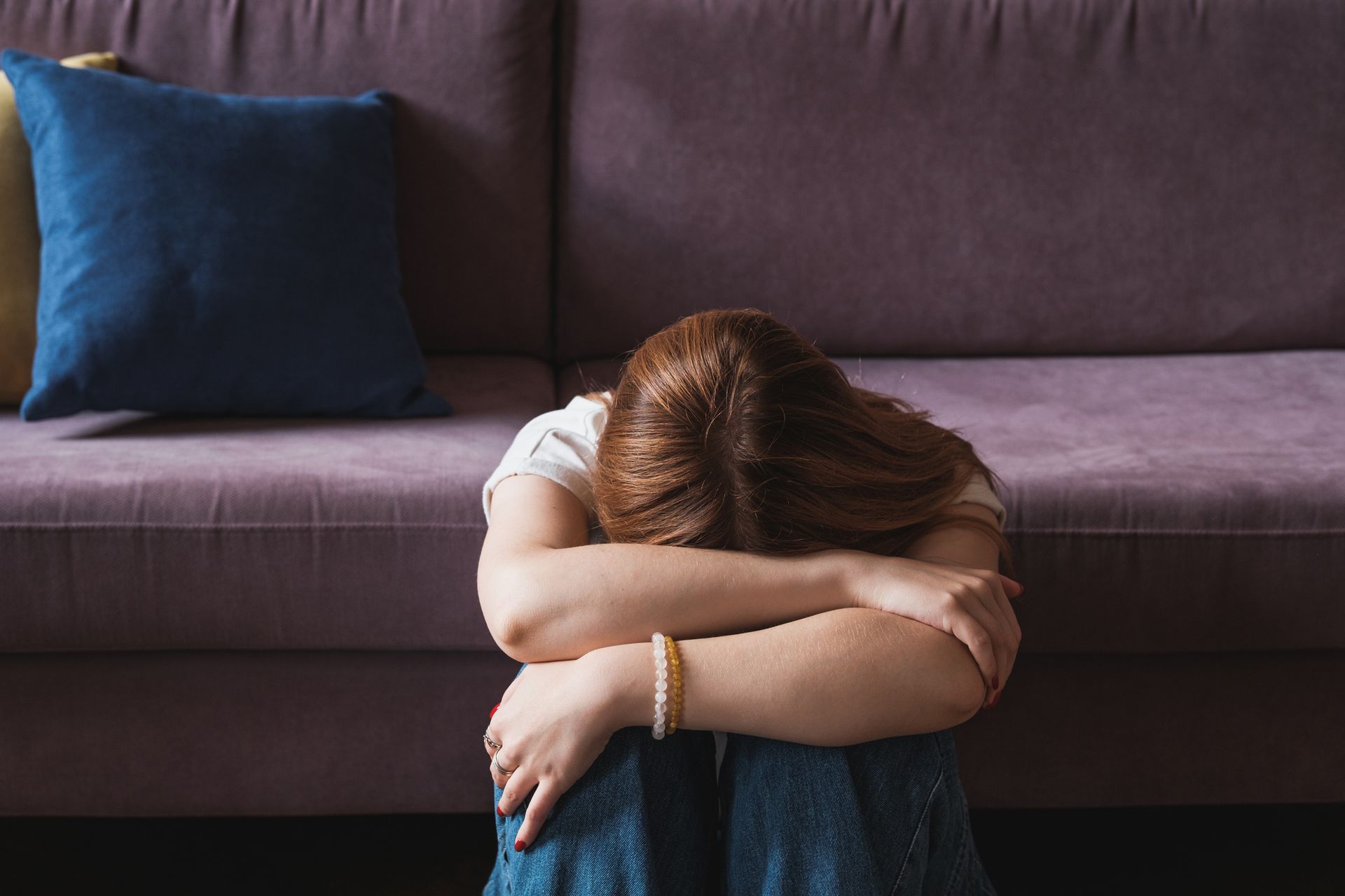 A Woman Is Sitting on The Floor with Her Head Down in Front of A Purple Couch. A Woman Is Sitting on The Floor with Her Head Down in Front of A Purple Couch.