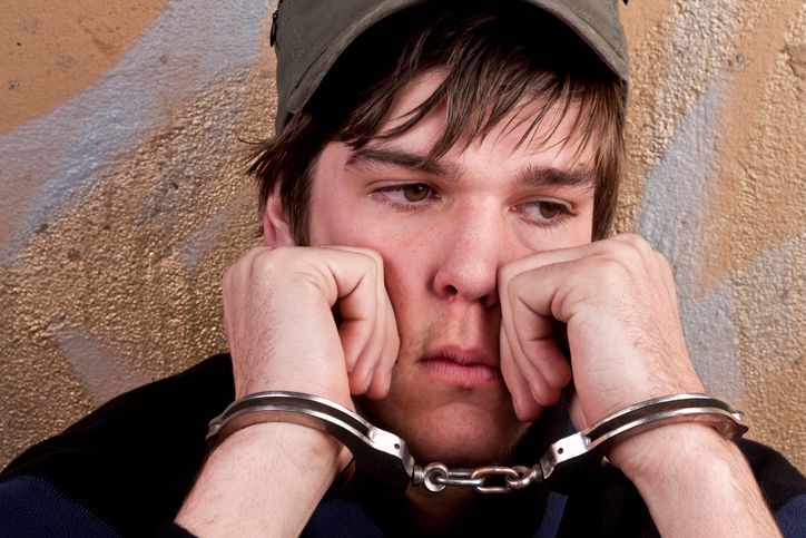 Teenager behind bar — Cohen Law Office — St. Eu Claire, WI A young man is wearing handcuffs and a hat.