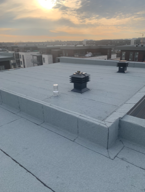 A roof with two chimneys on it and a view of a city.