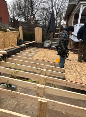 A man is standing on a wooden deck under construction.