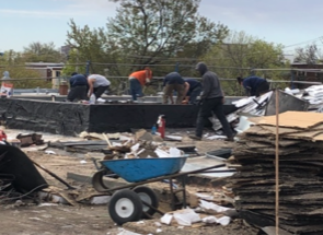 A group of men are working on a roof with a wheelbarrow in the foreground