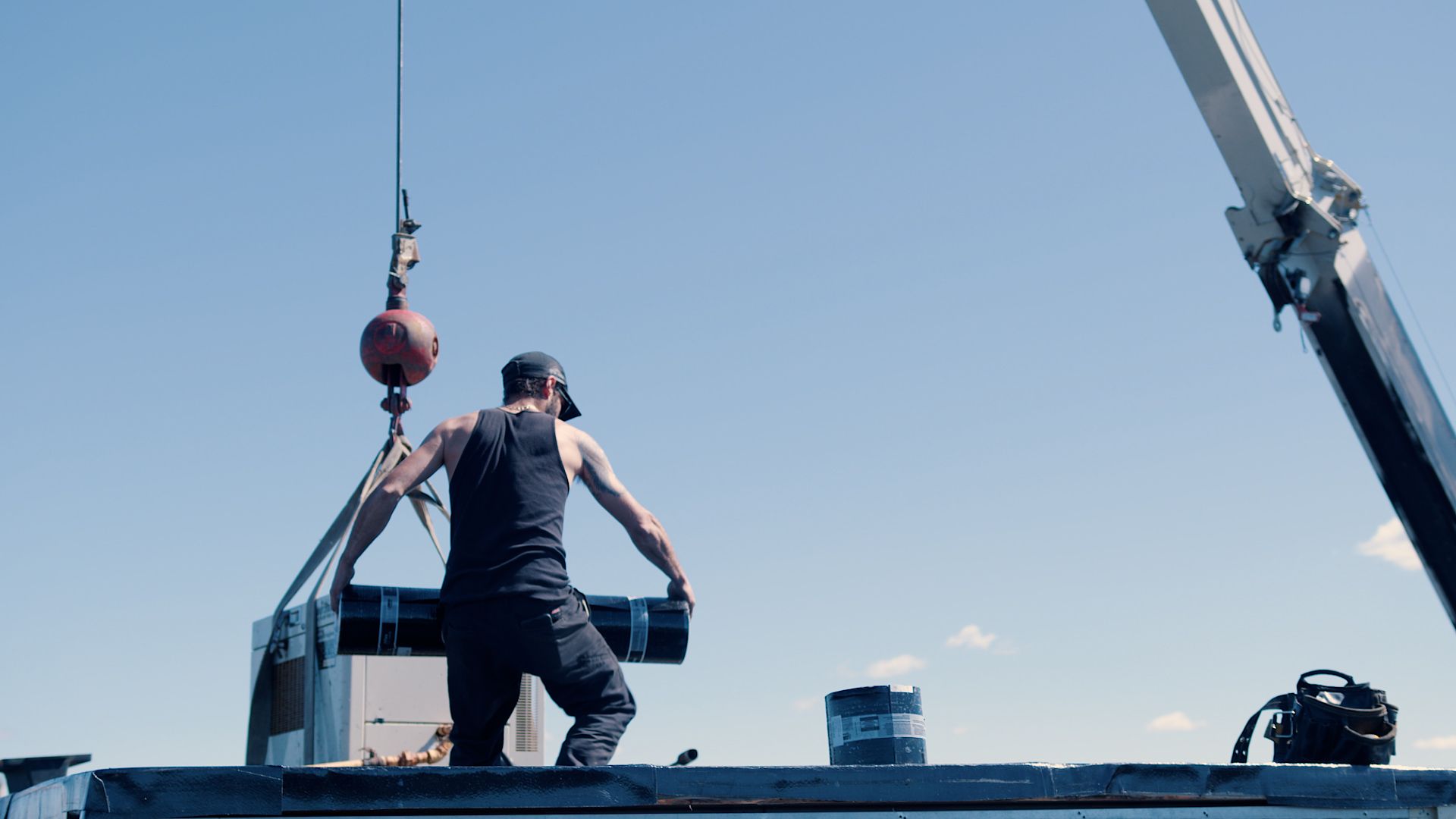 A man is standing on top of a boat with a crane in the background.