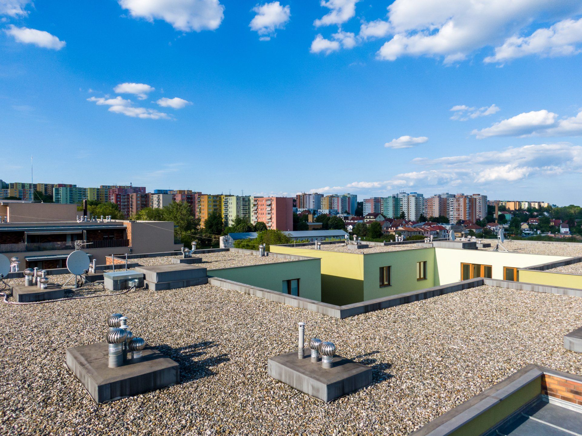 Un toit plat recouvert de gravier donnant sur un quartier résidentiel aux immeubles colorés, sous un ciel bleu.