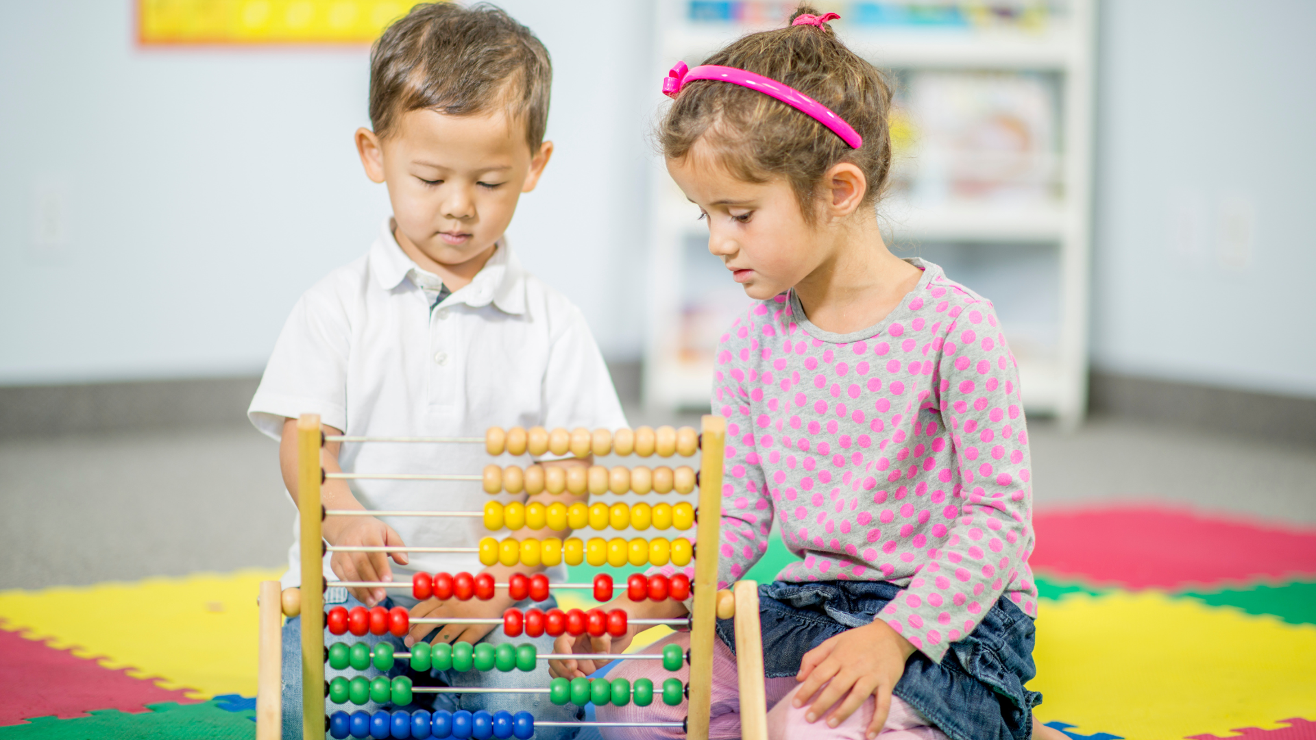 Two children playing with an abacus on a colorful classroom floor