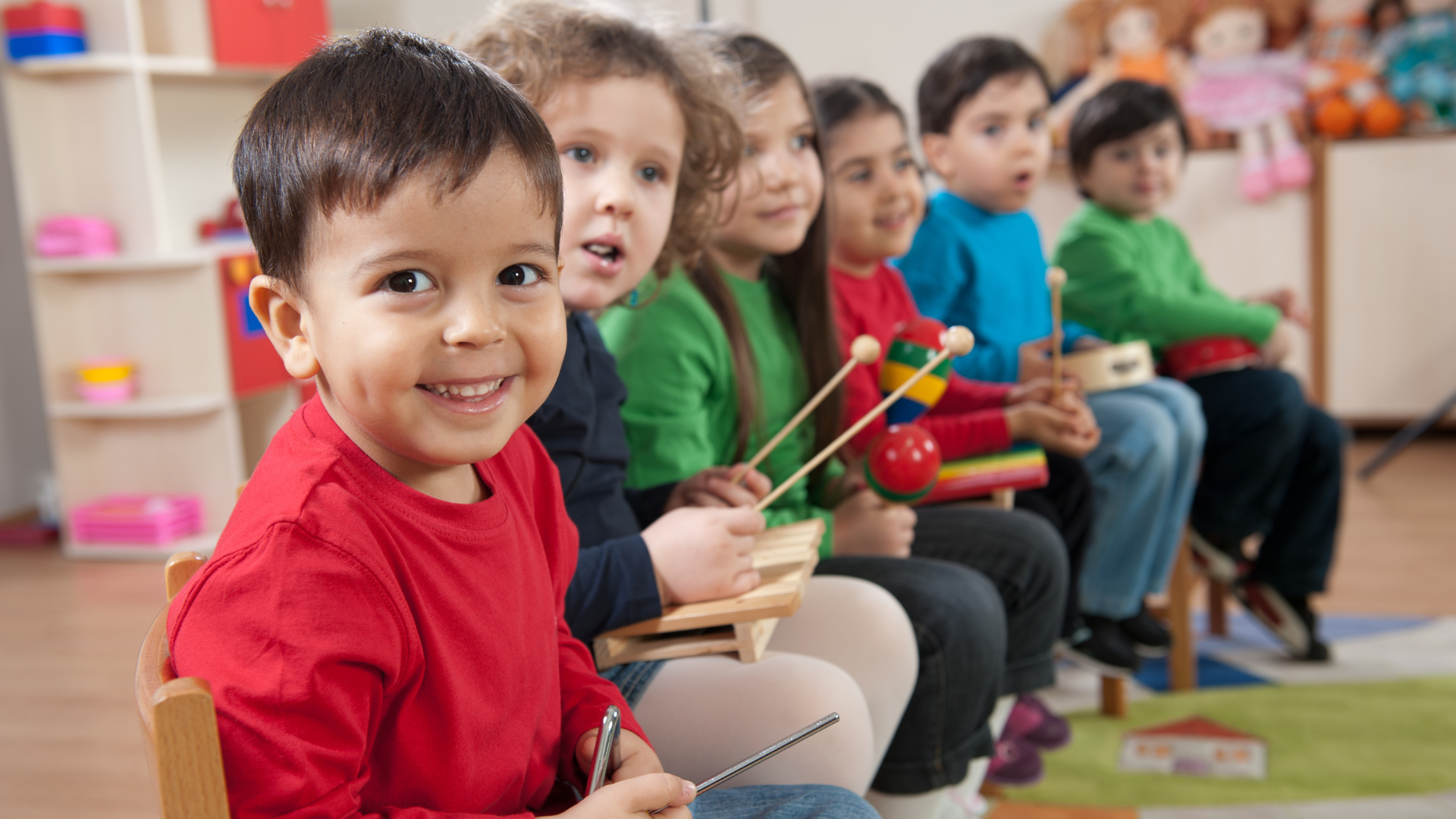 Children seated in a classroom, smiling and holding small percussion instruments