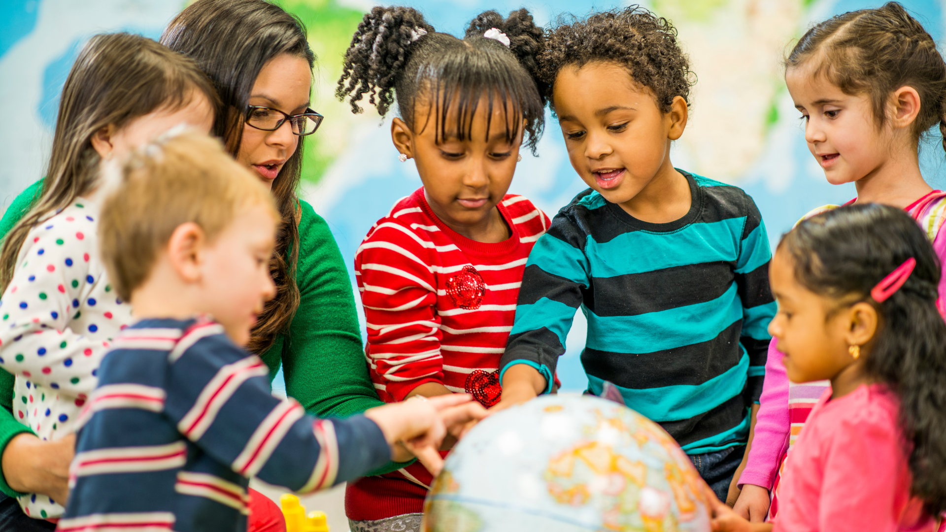 Children gathered around a globe, smiling and looking at it together in a classroom setting