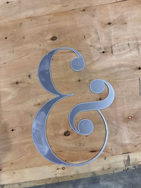 Metallic ampersand sign on a plywood wall, painted silver-blue.