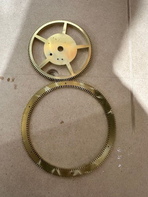 Two metal gears on a cardboard surface: a small spoked wheel above a large toothed ring.